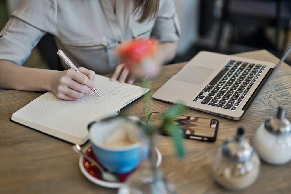 žena piše vodič za organski content marketing u rokovnik a pored laptopa na stolu